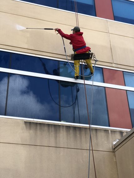 Professional building washer on high-rise rope pressure washing hospital building stone wall