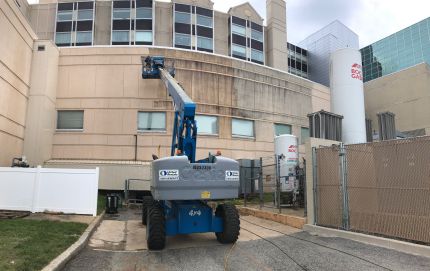 Expert washer on crane Power Washing Hospital stained walls clean